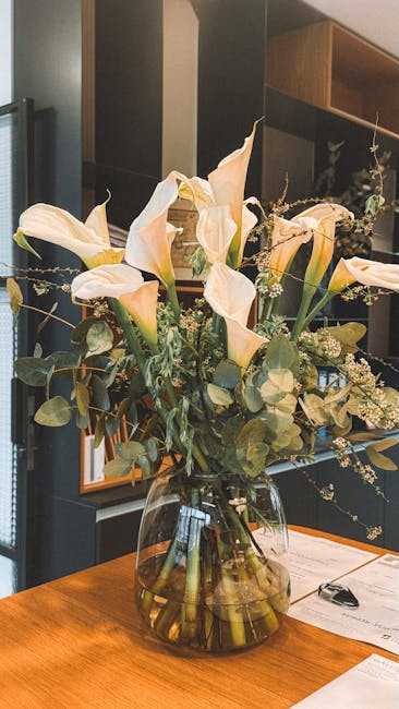A bouquet arrangement featuring large, creamy white calla lilies with elegant, trumpet-shaped blooms, complemented by sprigs of delicate white baby's breath and muted green eucalyptus leaves. The flow